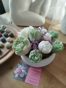 Composition florale en bougies dans les tons verts et blancs parsemés de petites fleurs séchées violettes.