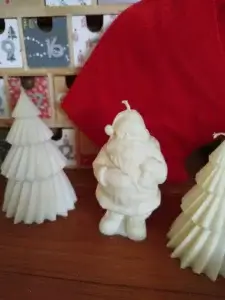 Bougie en forme de Père Noël placé à côté de deux sapins bougies avec un fond en décor rouge.