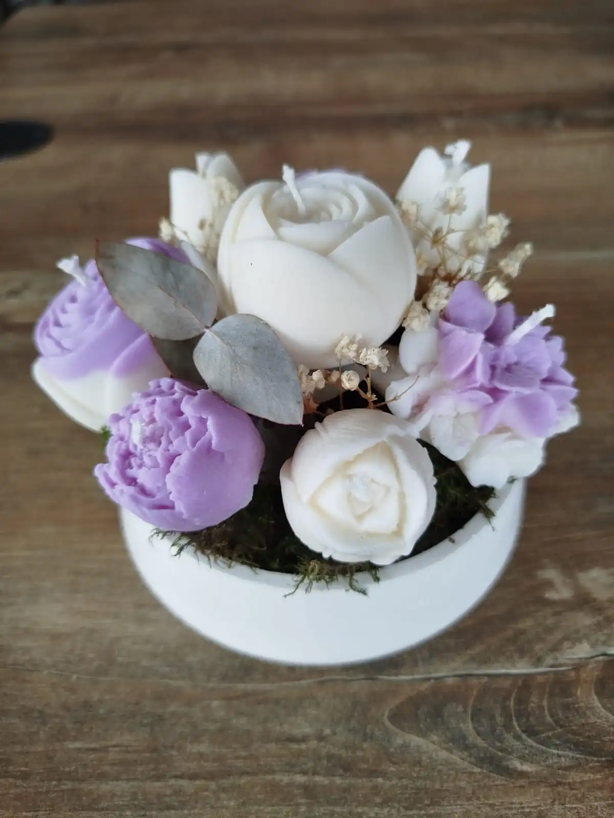 Composition de bougies en forme de fleurs de couleur parme avec des feuilles d'eucalyptus.