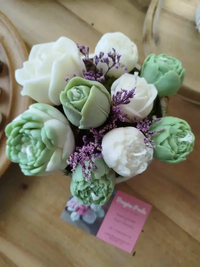 Composition florale en bougies. Les bougies de couleur vertes et blanches sont disposées dans un contenant rond en plâtre blanc.