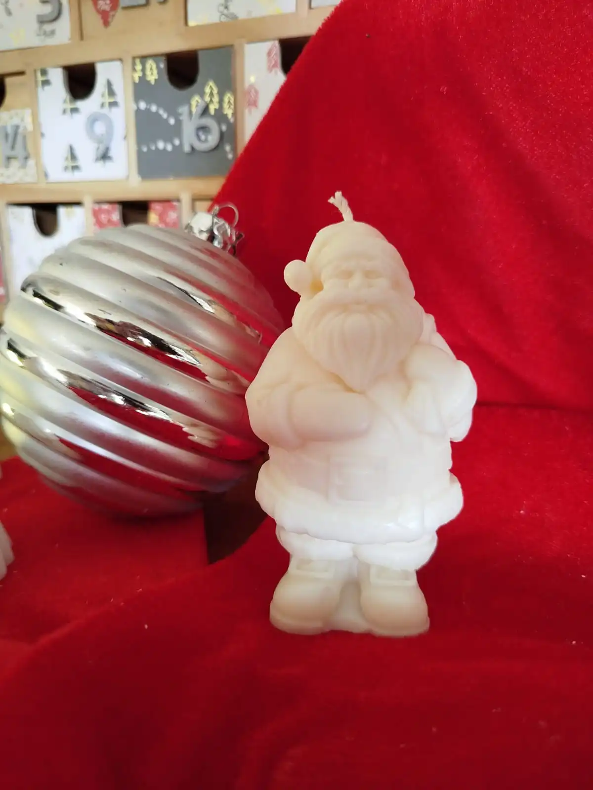 Bougie en forme de Père Noël placé à côté d'une boule argentée avec un fond en décor rouge.
