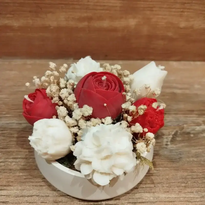 Composition florale à base de bougies en forme de fleurs de coloris rouge et crème.