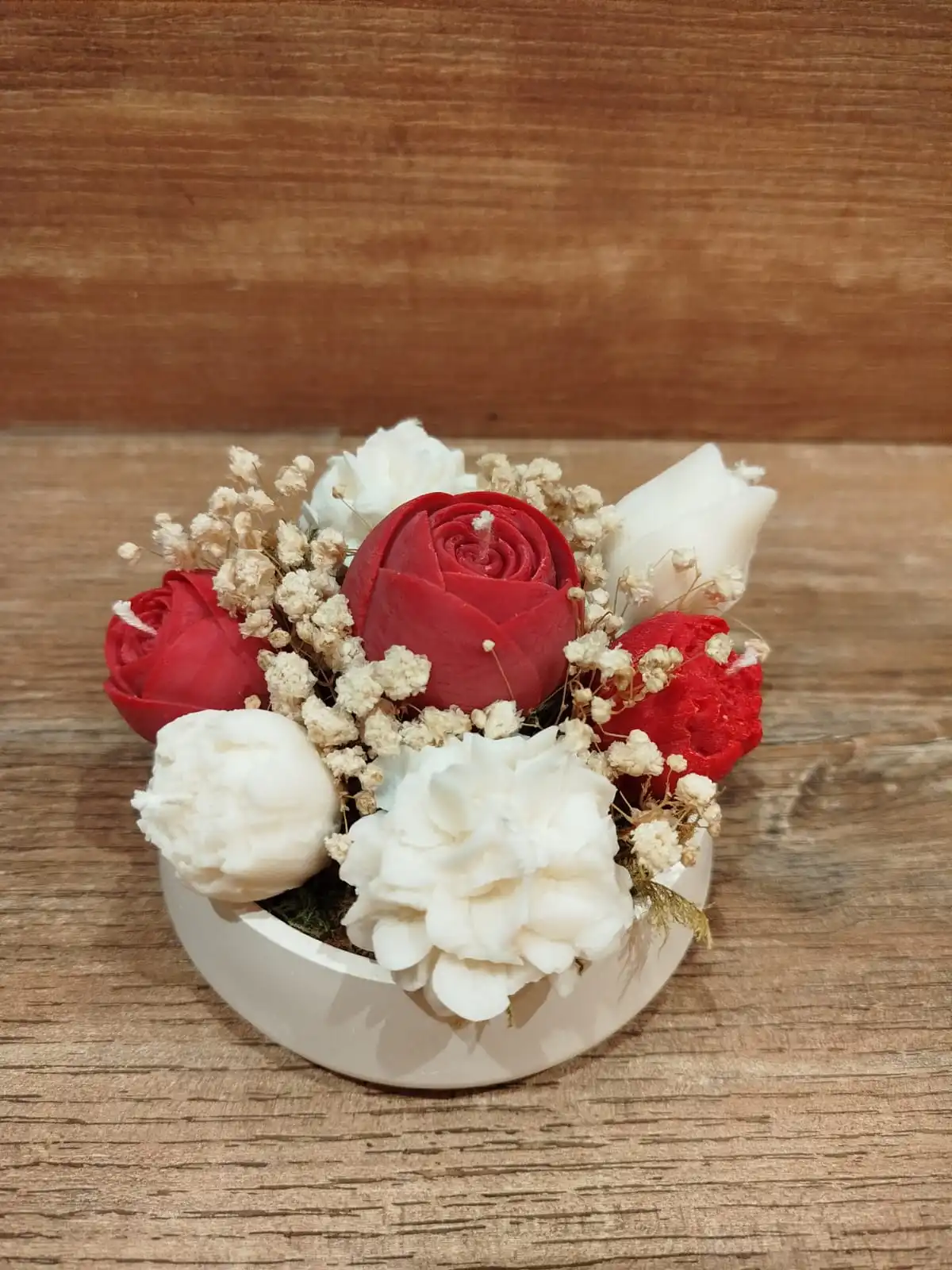 Composition florale à base de bougies en forme de fleurs de coloris rouge et crème.