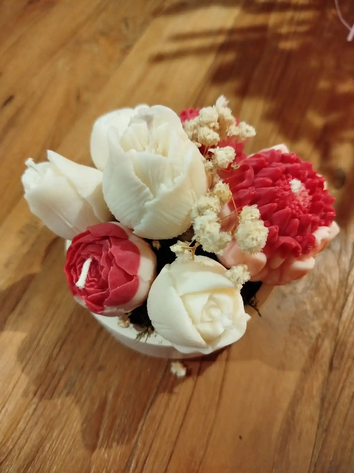 Des bougies en forme de fleurs de couleur rose rouge dans une coupelle en plâtre.