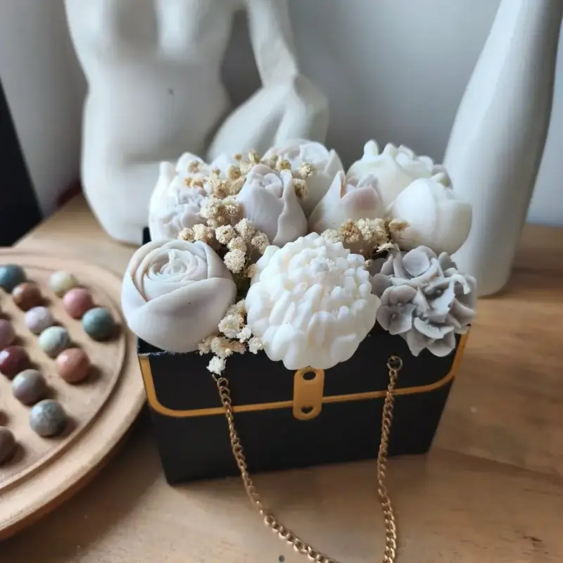 Bouquet de bougies dans les tons beige disposé dans un sac noir avec sa chainette dorée.
