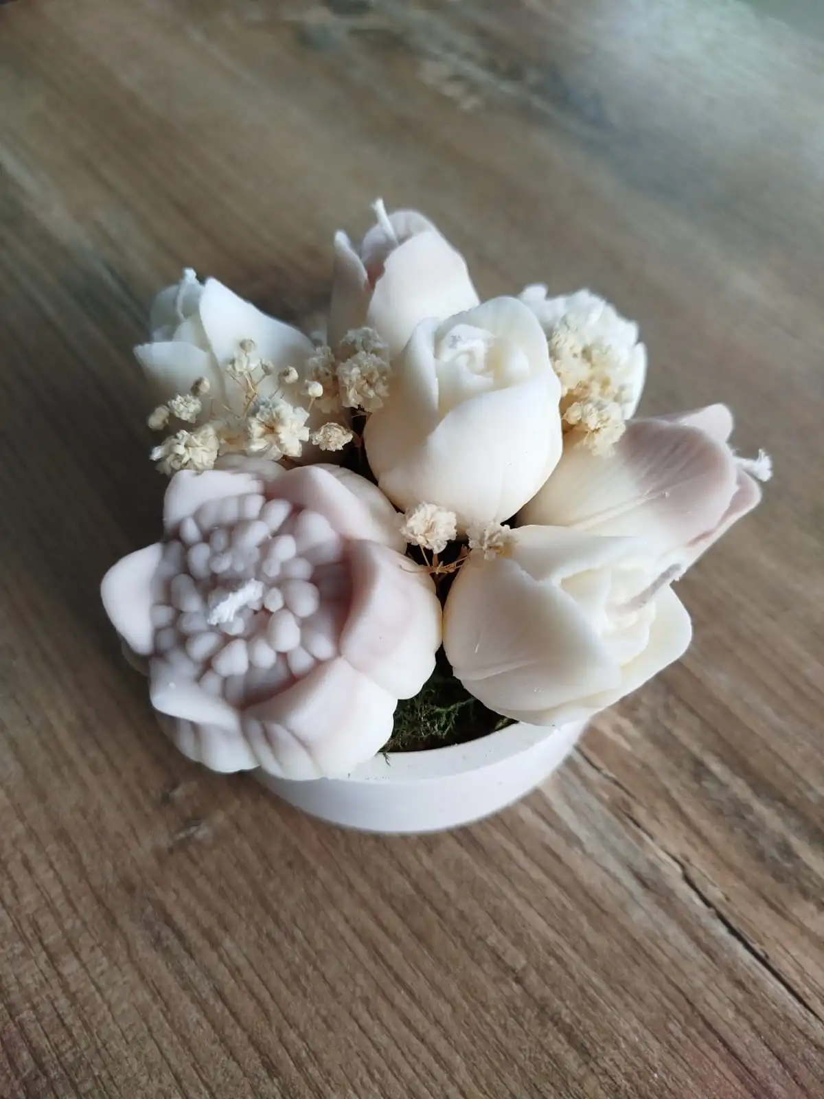 Une composition de bougies dans les tons beige posée sur un plan de travail en bois.