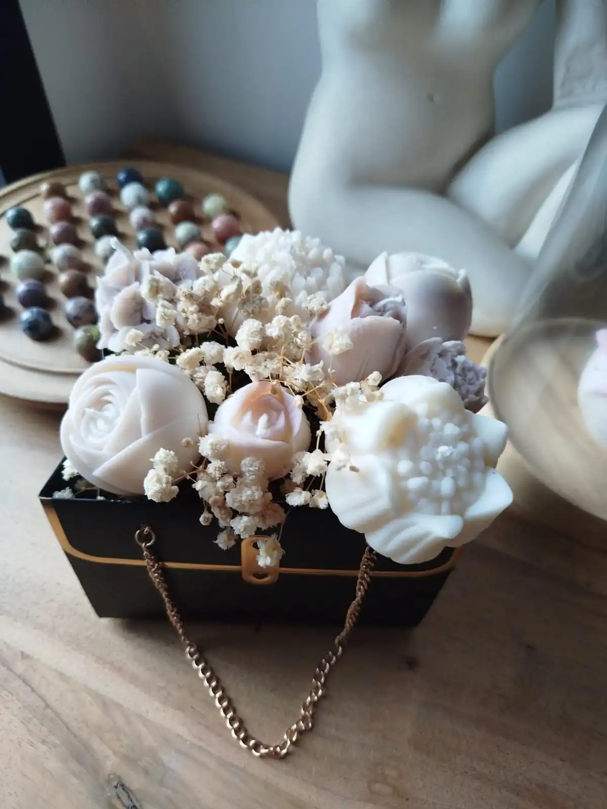 Sac noir contenant des bougies de couleur beige et cire naturelle, il est orné d'une chainette dorée.